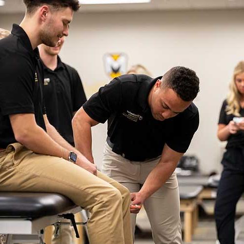 Two students practice checking on another's reflexes on the knee as a class demonstration